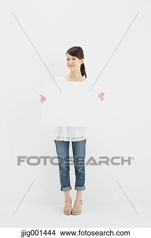 Picture - Japanese young woman in jeans and white shirt standing against white background. Fotosearch