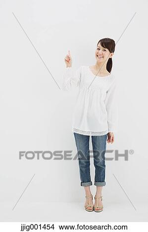 Picture - Japanese young woman in jeans and white shirt standing against white background. Fotosearch