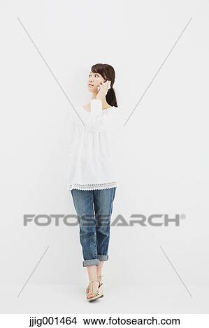 Japanese young woman in jeans and white shirt with smartphone standing against white background View Large Photo Image Picture - Japanese young woman in jeans and white shirt with smartphone standing against white background. Fotosearch