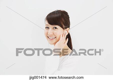 Japanese young woman in jeans and white shirt with earphones standing against white background View Large Photo Image Picture - Japanese young woman in jeans and white shirt with earphones standing against white background. Fotosearch