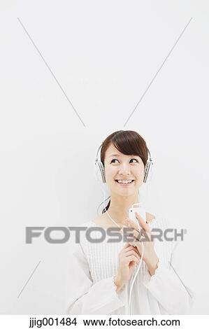Japanese young woman in jeans and white shirt with earphones standing against white background View Large Photo Image Picture - Japanese young woman in jeans and white shirt with earphones standing against white background. Fotosearch