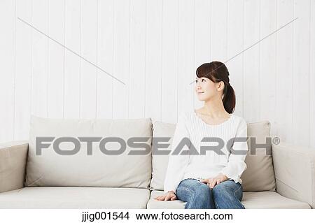 Picture - Japanese young woman in jeans and white shirt on the sofa. Fotosearch