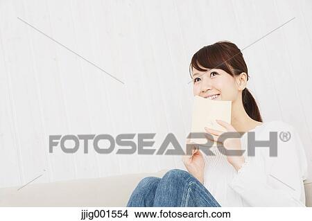 Japanese young woman in jeans and white shirt with a book on the sofa View Large Photo Image Picture - Japanese young woman in jeans and white shirt with a book on the sofa. Fotosearch