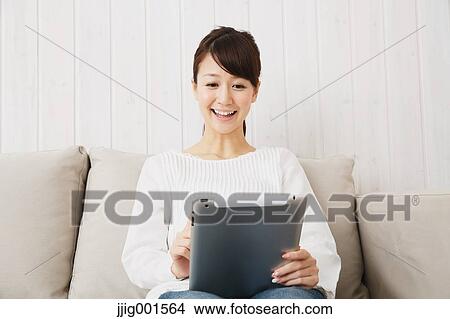 Japanese young woman in jeans and white shirt with tablet on the sofa View Large Photo Image Picture - Japanese young woman in jeans and white shirt with tablet on the sofa. Fotosearch