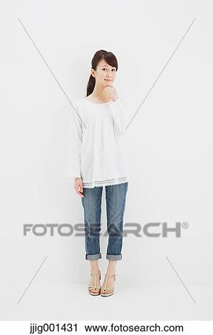 Stock Image - Japanese young woman in jeans and white shirt standing against white background. Fotosearch
