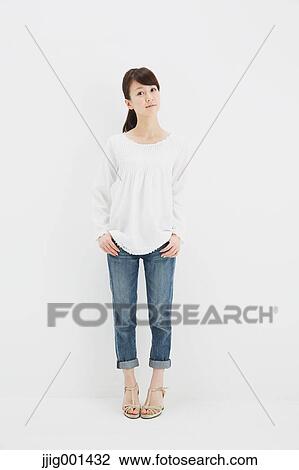 Stock Image - Japanese young woman in jeans and white shirt standing against white background. Fotosearch