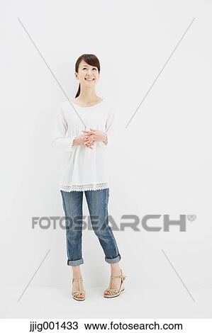 Stock Image - Japanese young woman in jeans and white shirt standing against white background. Fotosearch