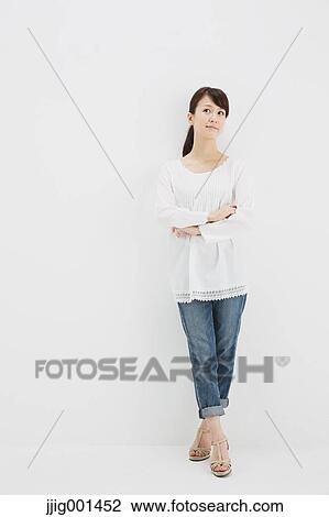 Stock Image - Japanese young woman in jeans and white shirt standing against white background. Fotosearch