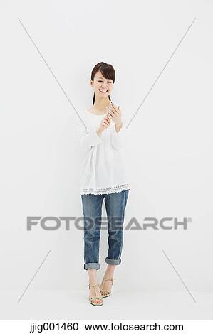 Japanese young woman in jeans and white shirt with smartphone standing against white background View Large Photo Image Stock Image - Japanese young woman in jeans and white shirt with smartphone standing against white background. Fotosearch