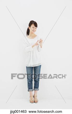 Japanese young woman in jeans and white shirt with smartphone standing against white background View Large Photo Image Stock Image - Japanese young woman in jeans and white shirt with smartphone standing against white background. Fotosearch