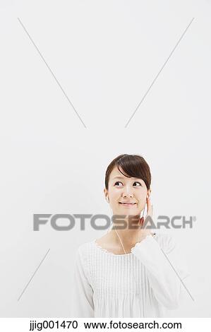 Stock Image - Japanese young woman in jeans and white shirt with earphones standing against white background. Fotosearch