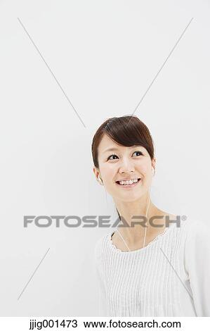 Stock Image - Japanese young woman in jeans and white shirt with earphones standing against white background. Fotosearch