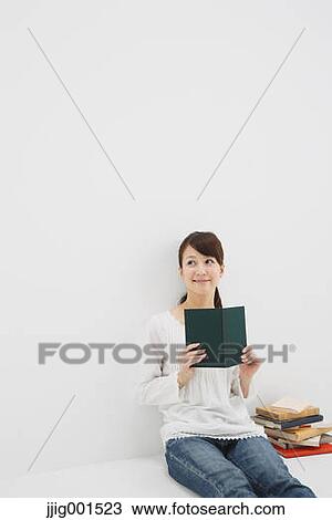 Stock Image - Japanese young woman in jeans and white shirt with a book against white background. Fotosearch