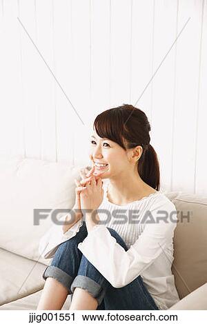 Stock Image - Japanese young woman in jeans and white shirt on the sofa. Fotosearch