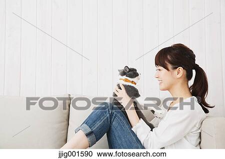 Stock Image - Japanese young woman in jeans and white shirt with cat on the sofa. Fotosearch