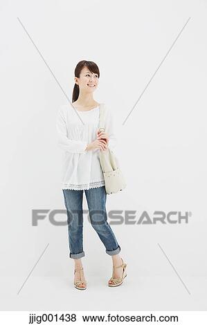 Stock Photo - Japanese young woman in jeans and white shirt standing against white background. Fotosearch
