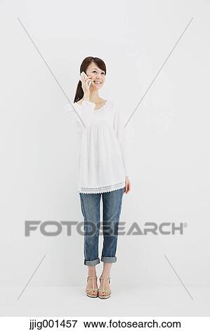 Stock Photo - Japanese young woman in jeans and white shirt with smartphone standing against white background. Fotosearch