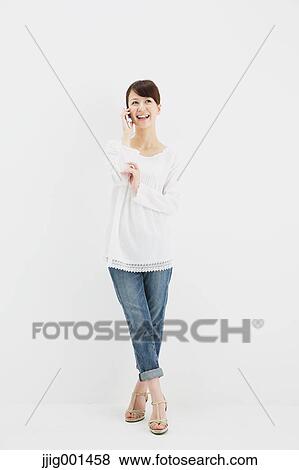 Stock Photo - Japanese young woman in jeans and white shirt with smartphone standing against white background. Fotosearch