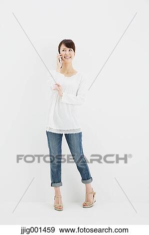 Japanese young woman in jeans and white shirt with smartphone standing against white background View Large Photo Image Stock Photo - Japanese young woman in jeans and white shirt with smartphone standing against white background. Fotosearch