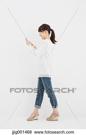 Japanese young woman in jeans and white shirt with smartphone standing against white background View Large Photo Image Stock Photo - Japanese young woman in jeans and white shirt with smartphone standing against white background. Fotosearch
