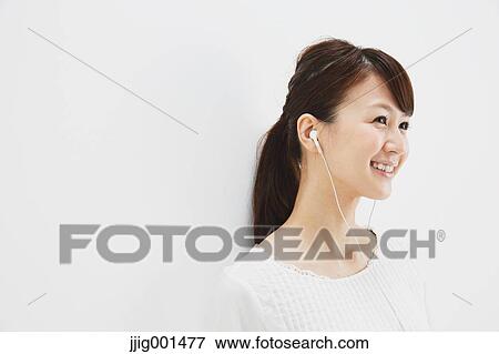Stock Photo - Japanese young woman in jeans and white shirt with earphones standing against white background. Fotosearch