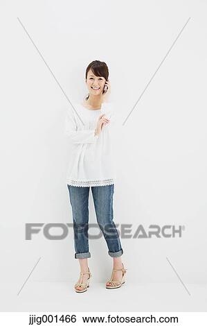 Japanese young woman in jeans and white shirt with smartphone standing against white background View Large Photo Image Stock Photograph - Japanese young woman in jeans and white shirt with smartphone standing against white background. Fotosearch