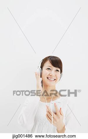 Stock Photograph - Japanese young woman in jeans and white shirt with earphones standing against white background. Fotosearch