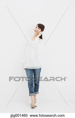 Stock Photography - Japanese young woman in jeans and white shirt with smartphone standing against white background. Fotosearch