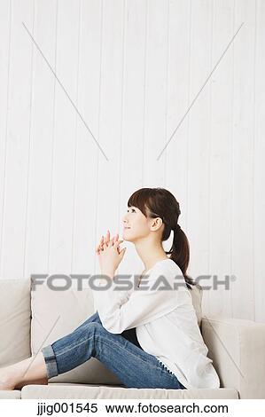 Stock Photography - Japanese young woman in jeans and white shirt on the sofa. Fotosearch