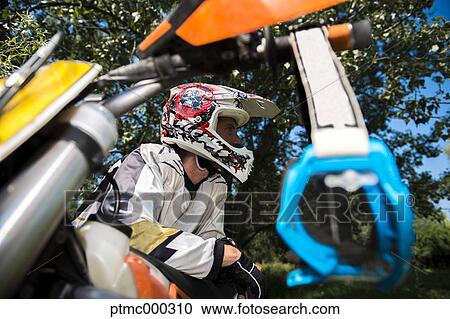 Stock Image - Young Man Relaxing Besides Motocross Bike in Countryside. Fotosearch