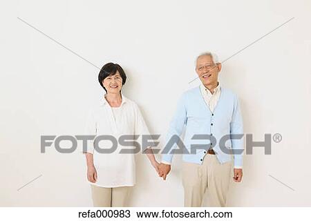 Stock Image - Senior adult Japanese couple against white wall. Fotosearch