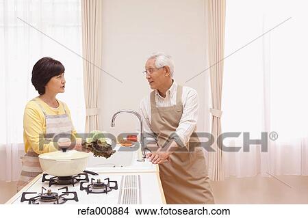 Picture - Senior adult Japanese couple in the kitchen. Fotosearch
