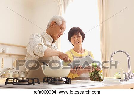 Picture - Senior adult Japanese couple in the kitchen. Fotosearch