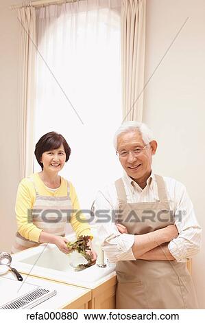 Stock Image - Senior adult Japanese couple in the kitchen. Fotosearch