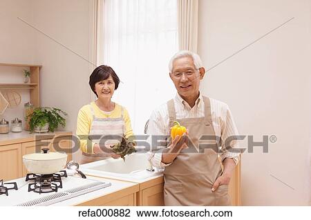 Stock Image - Senior adult Japanese couple in the kitchen. Fotosearch