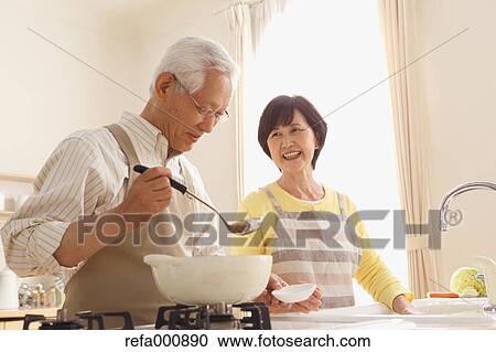 Stock Image - Senior adult Japanese couple in the kitchen. Fotosearch