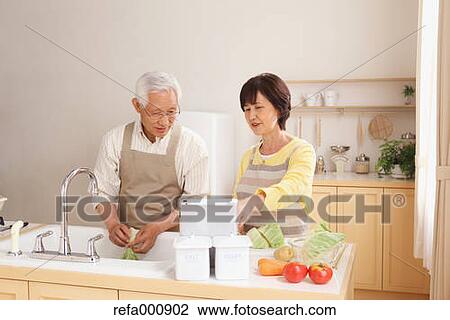 Stock Image - Senior adult Japanese couple in the kitchen. Fotosearch