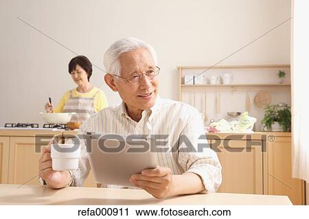Stock Image - Senior adult Japanese couple in the kitchen. Fotosearch