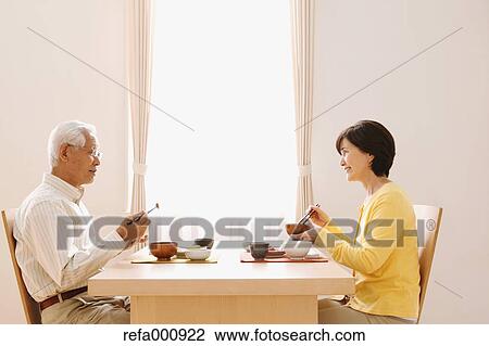 Stock Image - Senior adult Japanese couple in the kitchen. Fotosearch