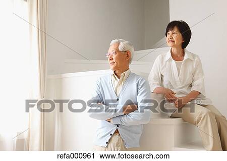 Stock Image - Senior adult Japanese couple in the living room. Fotosearch