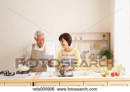 Stock Photograph - Senior adult Japanese couple in the kitchen. Fotosearch