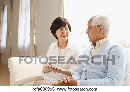 Stock Image - Senior adult Japanese couple on the sofa. Fotosearch