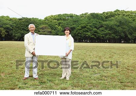 Stock Image - Senior adult Japanese couple with whiteboard in a park. Fotosearch
