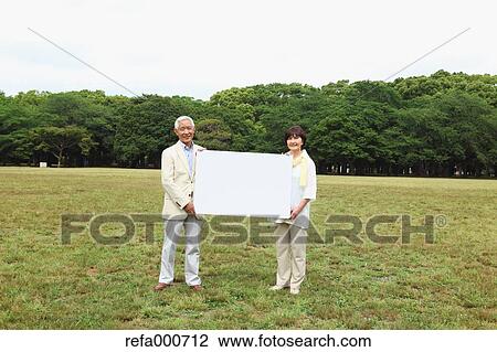 Stock Image - Senior adult Japanese couple with whiteboard in a park. Fotosearch