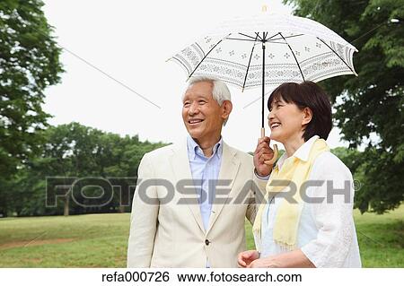 Stock Photograph - Senior adult Japanese couple with parasol in a park. Fotosearch