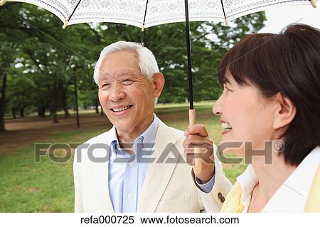 Stock Photography - Senior adult Japanese couple with parasol in a park. Fotosearch