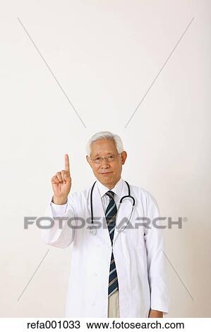 Stock Image - Senior adult Japanese doctor against white wall. Fotosearch