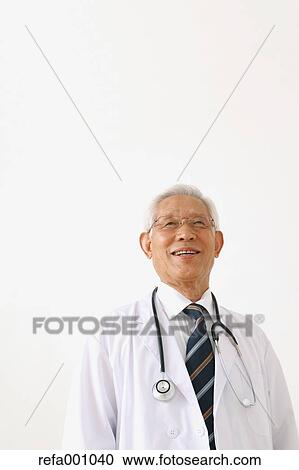 Stock Image - Senior adult Japanese doctor against white wall. Fotosearch
