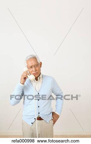 Stock Photo - Senior adult Japanese man with phone against white wall. Fotosearch
