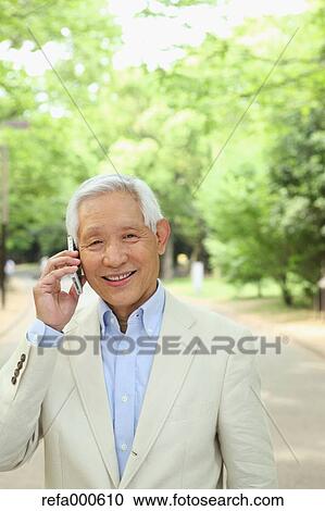 Stock Image - Senior adult Japanese man with smartphone in a park. Fotosearch